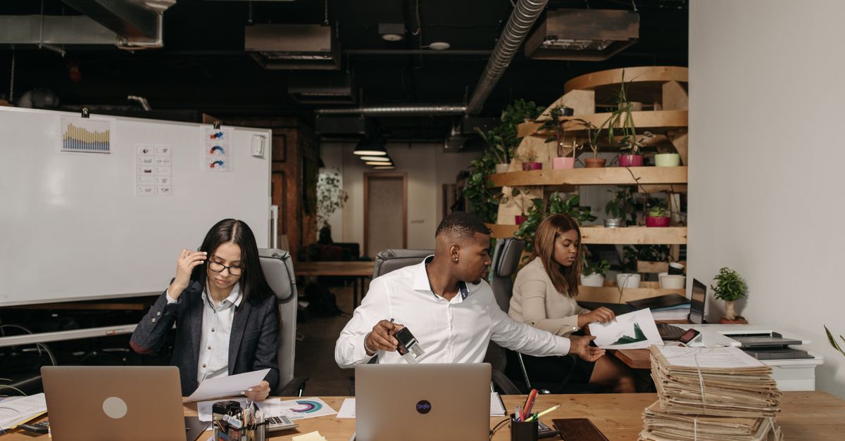 Diverses Team arbeitet in modernem Büro mit Laptops und Dokumenten zusammen.