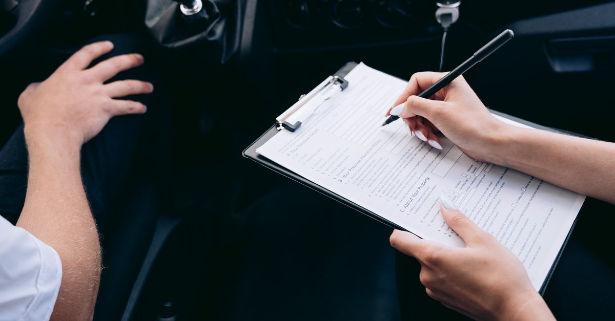 Person schreibt auf einem Klemmbrett im Auto, Hände neben dem Schalthebel sichtbar